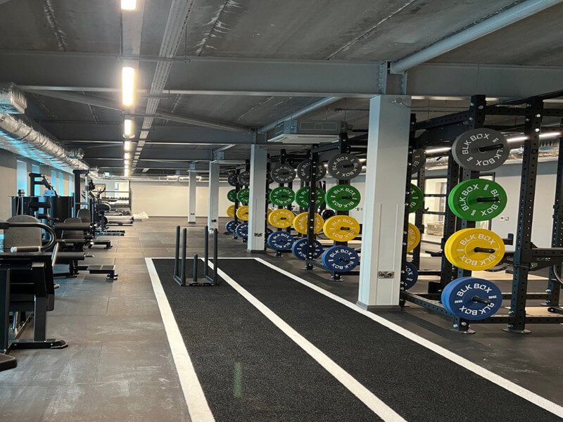 A side-by-side view of Gym Turf with a prowler sled and a rubber floor with a barbell.