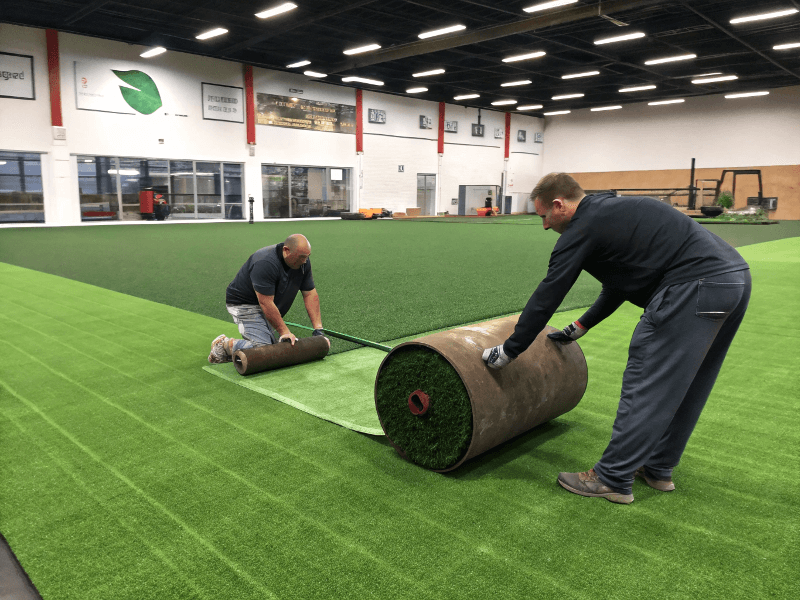 Ein Installationsteam mit einer schweren Walze auf einem neuen Turnhallenrasen